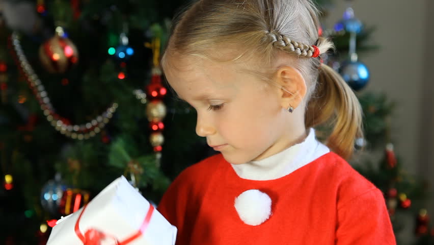 Child Looking with Interest at her Christmas Gift at the Christmas Tree, Little Girl Near Christmas Tree