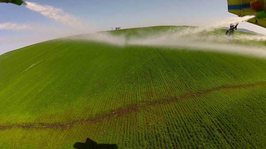Spray leaving the nozzles of a spray plane/crop duster on a field of wheat