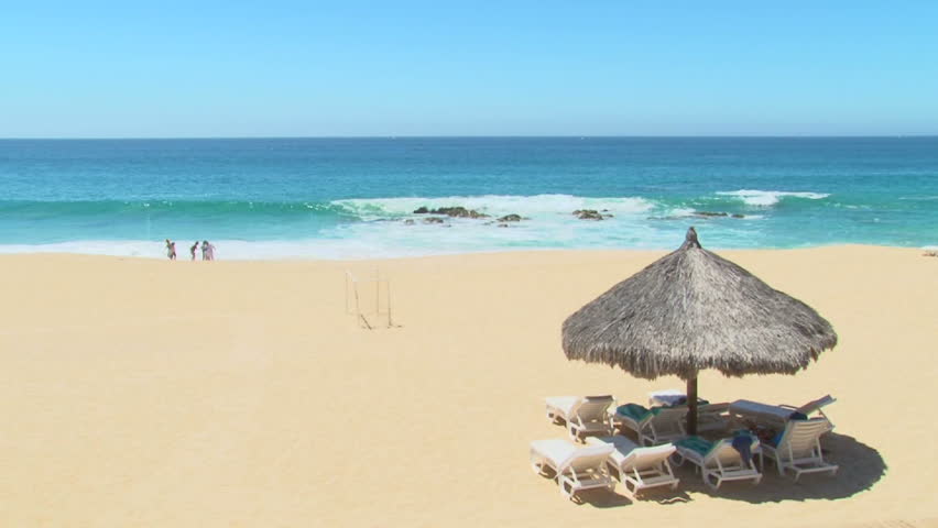 Unrecognizable people enjoy perfect blue sky day at the beach in Cabo San Lucas, Mexico by resort.