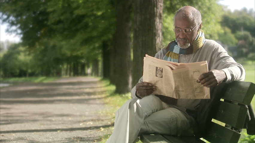 A man sitting on a bench reading a newspaper