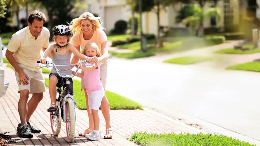 Caucasian parents and child encouraging older sister on bicycle