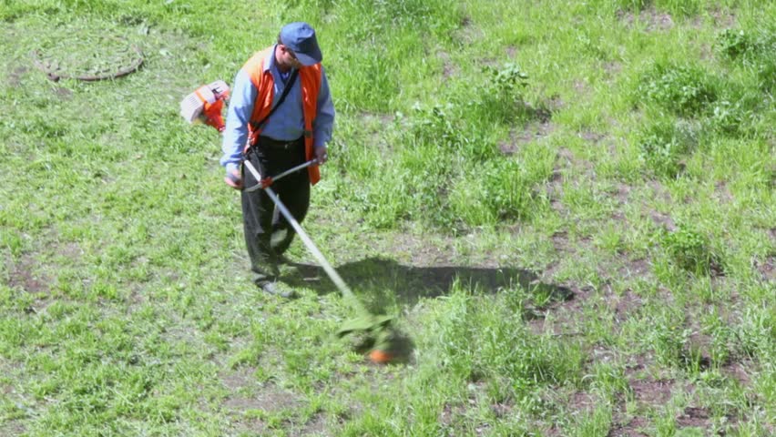 Man walks with lawn mower and mows grass at sunny summer day