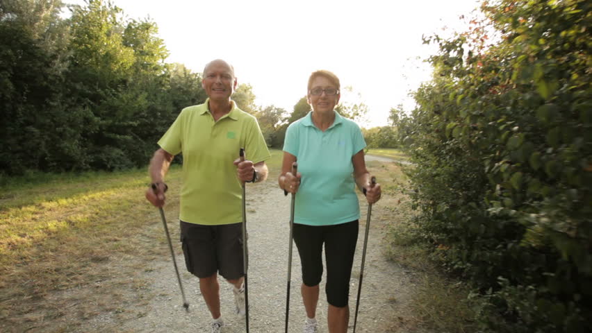 tracking shot happy smiling retirees nordic walking in late afternoon
