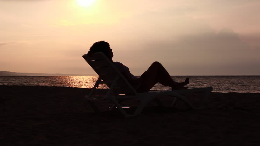 Mother and daughter hugging and kissing on a lounge by the sea. Sunrise in the background.