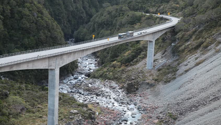 Vehicles, truck and cars drive slow over long bridge across canyon in New Zealand