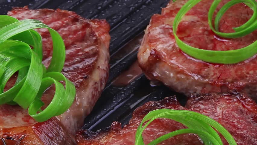 fresh grilled bloody beef steaks on black grill plate with green leaves isolated on white background