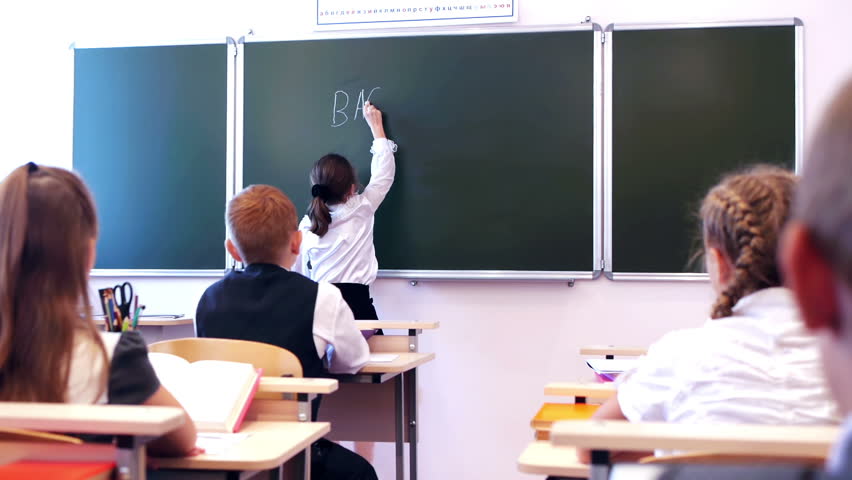 Adorable schoolgirl writing text back to school in the classroom