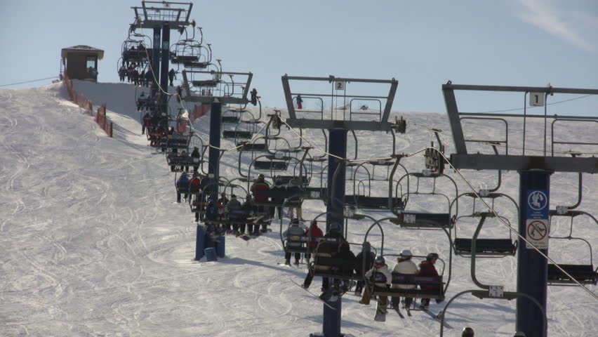 A ski lift is slowly transporting people to the top of the ski hill. (High Definition)