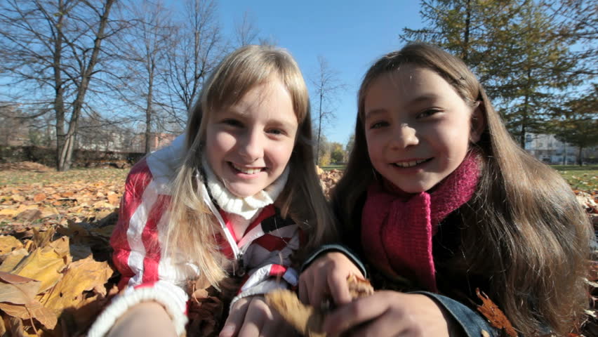 Pretty little classmates lying on the ground covered with fallen leaves and looking at the camera