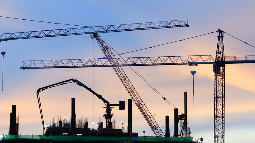 Cranes work on construction site after sunset, time lapse