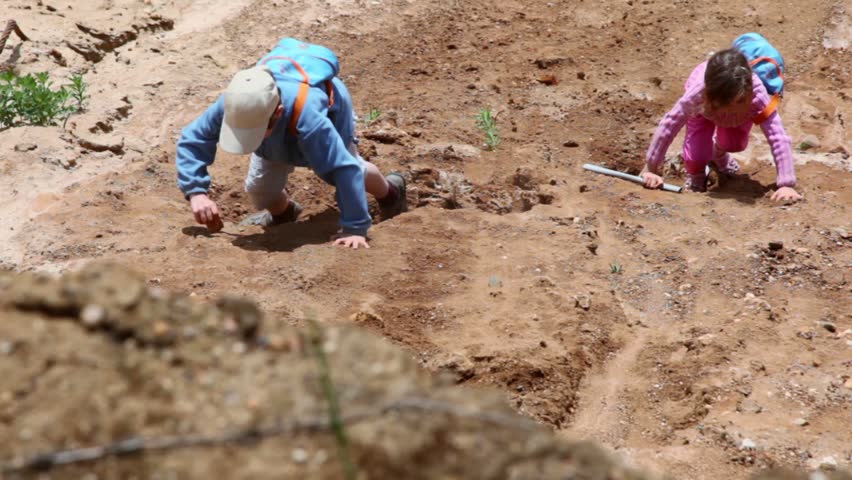 Two kids brother with little sister climb on ground slope, girl use stick and boy throws stone, view from above