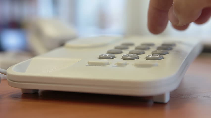 Dialing telephone number on desk phone by finger. Close up view