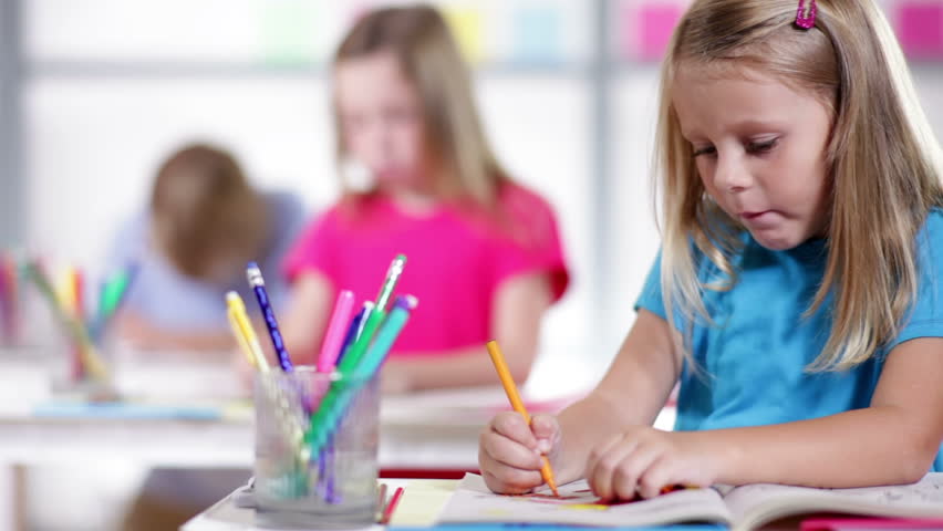 Cute little kindergarten child working at her desk is final focus of camera dolly movement.