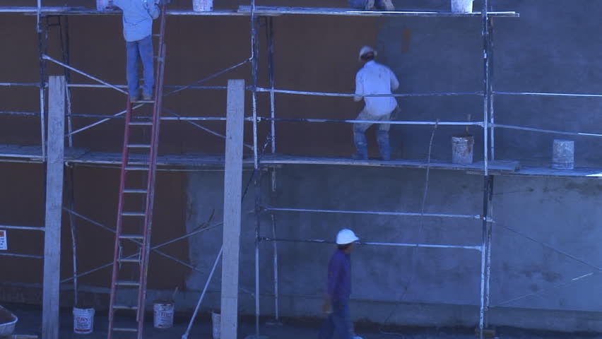 Stucco workers use scaffolding and ladders to apply skin coat to building