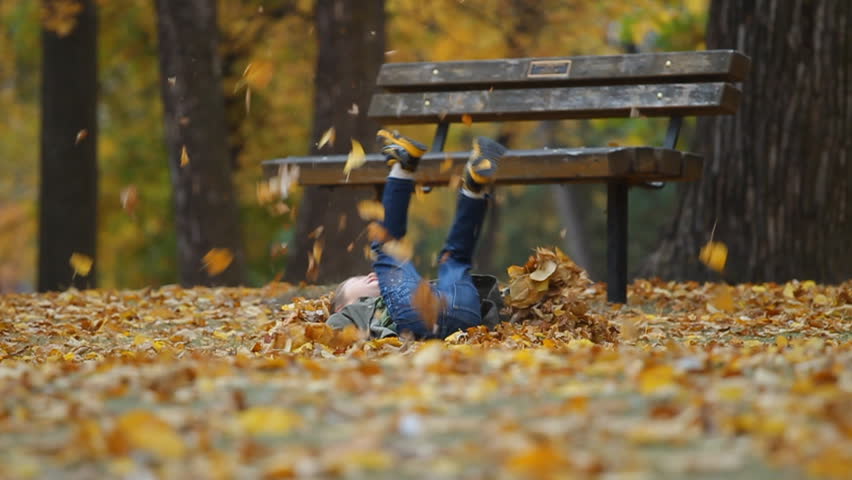 Running seven year old boy throws autumn leaves and falls to the ground. slow motion. 