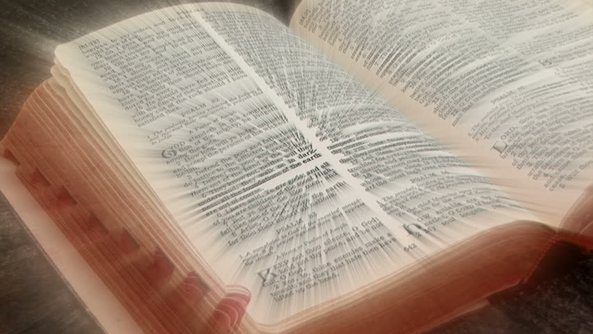 The pages of a Bible fanned back and forth by the wind, with rays of light coming from the bible pages.