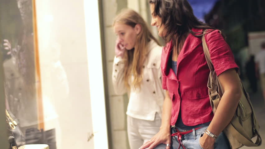 Young women looking at shop exhibition, evening, steadycam shot
