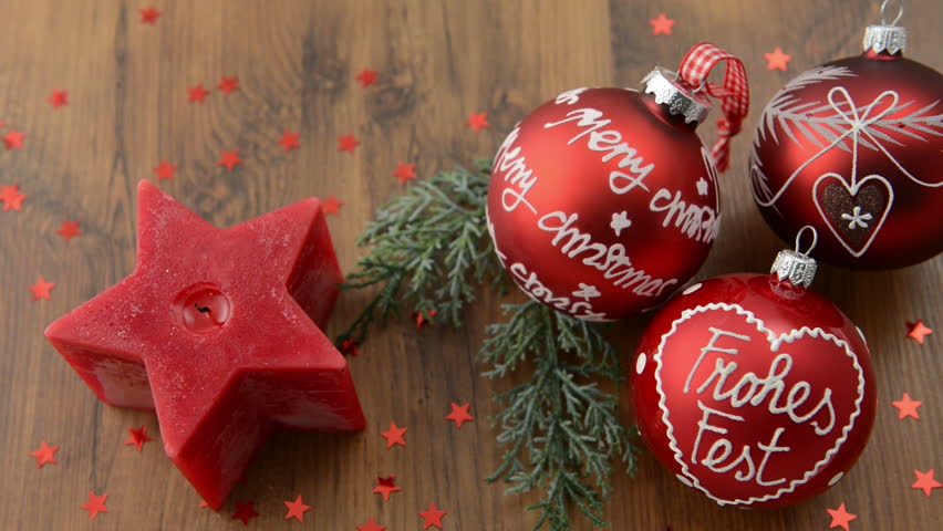 Christmas candle in star shape is lit with a match. In addition, a fir twig lies with three Christmas balls with the words "Merry Christmas" and german "Frohes Fest". 