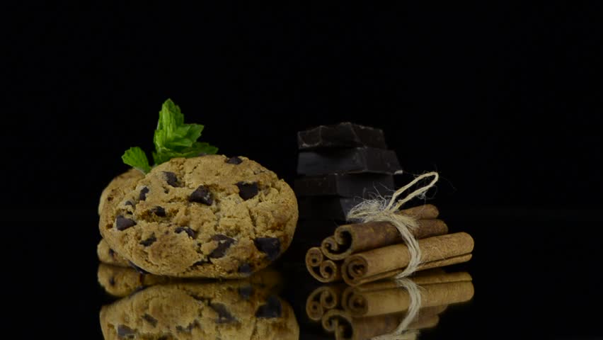 Chocolate cookies with green mint leaves rotating on black background.
