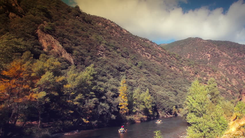 panomic view of a river in the Pyrenees (Catalonia-Spain) with group of peaople doing rafting . Warm colors. 
