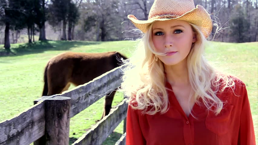 Cowgirl walks down a fence line. slow motion. 