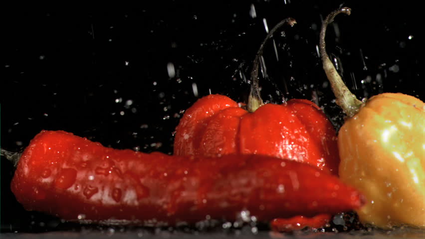 Drops in super slow motion falling on spicy vegetables against a black background