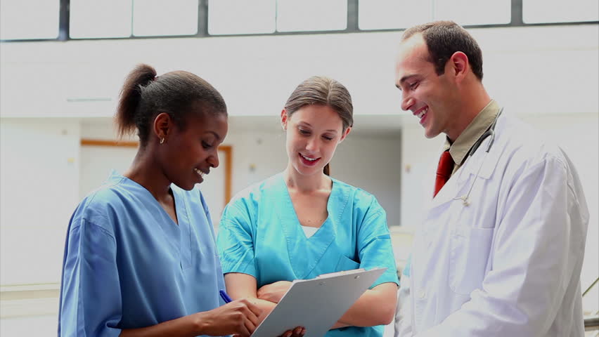 Smiling doctor listening to a nurse holding a clipboard in hospital corridor