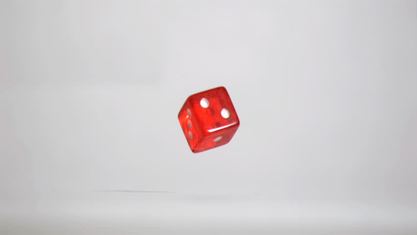 One red dice in super slow motion turning near the floor against a grey background