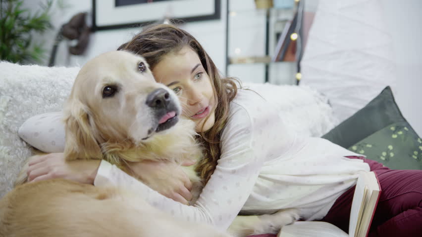 Attractive young woman at home is stroking and snuggling with her pet dog. In slow motion.