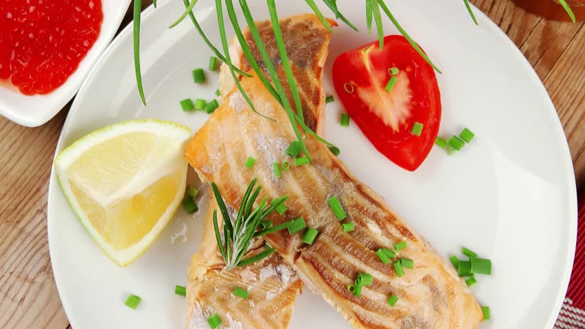 savory sea fish : baked salmon strips with green vegetable salad and tomatoes red caviar in white bowl grinder and cutlery on wooden table