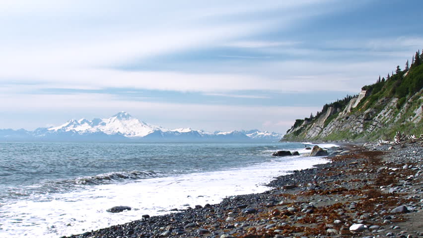 The waters of the Cook Inlet lap ceaselessly at a gravel and sand beach, the bluffs standing sentinel, while across the inlet Mt. Illiamna looms.