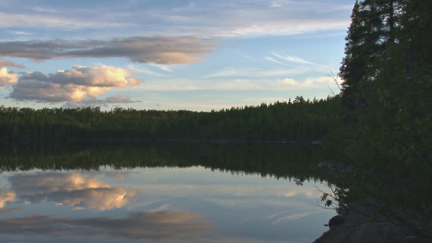 Panning left across an expansive vista of late afternoon/early evening clouds reflected in a mountain lake.