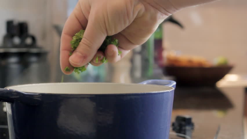 Chef adding fresh chopped herbs to cooking pot on stove