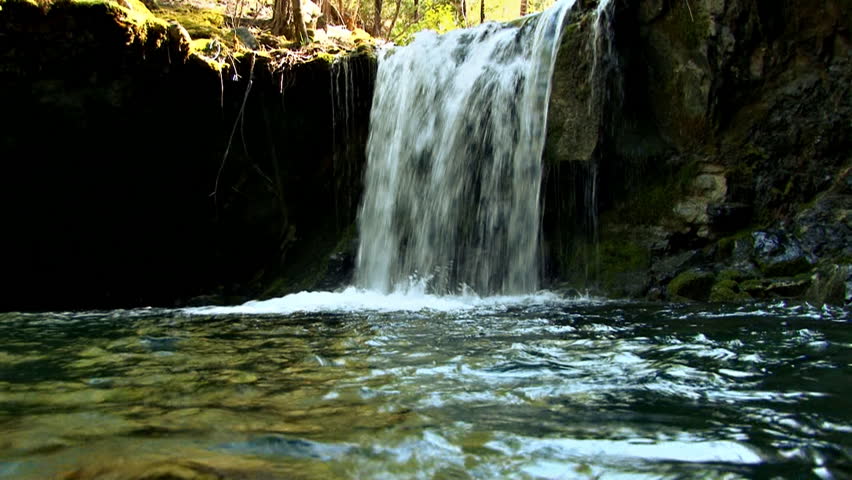 Small waterfall in creek, shot at water level, in a small grotto or cave with moss-covered rocks.