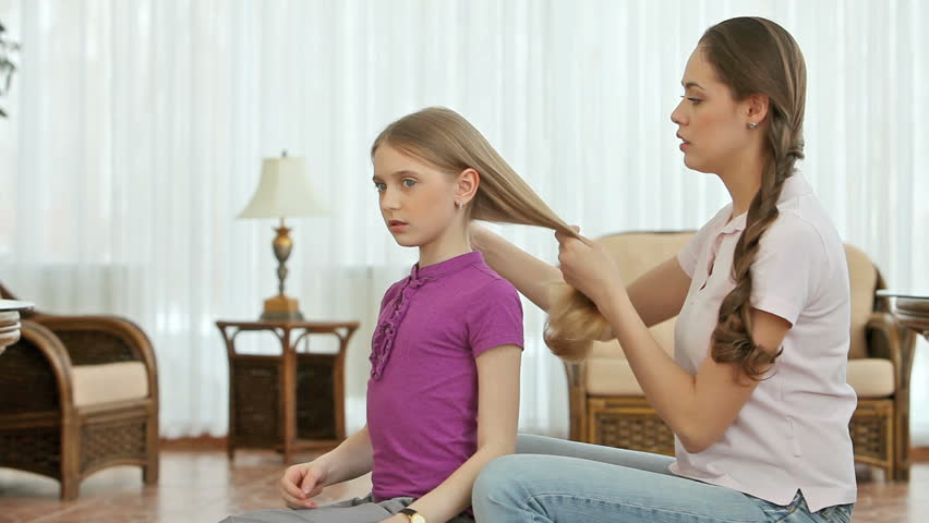Girl combing and braiding her little sisterâs hair