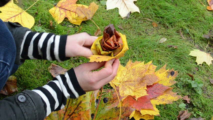 Woman hands make decor flower from beautiful autumn tree leaves.