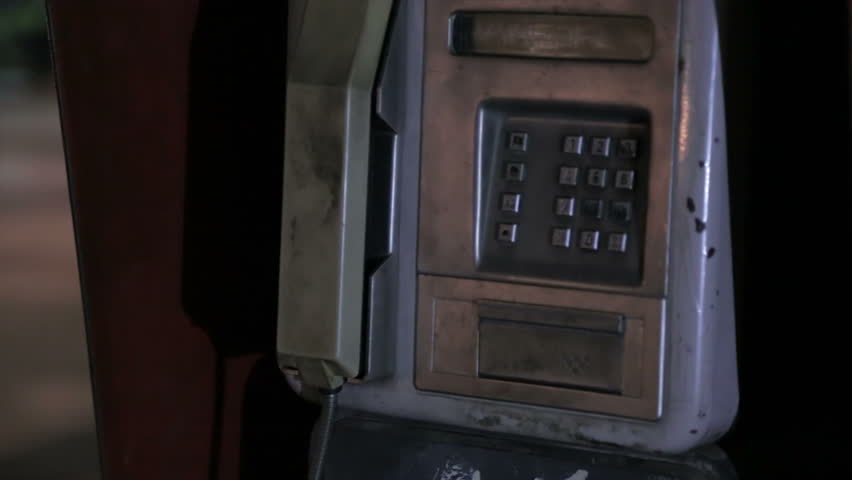 Man's hand holding the handset of a public telephone and dialing the phone number 