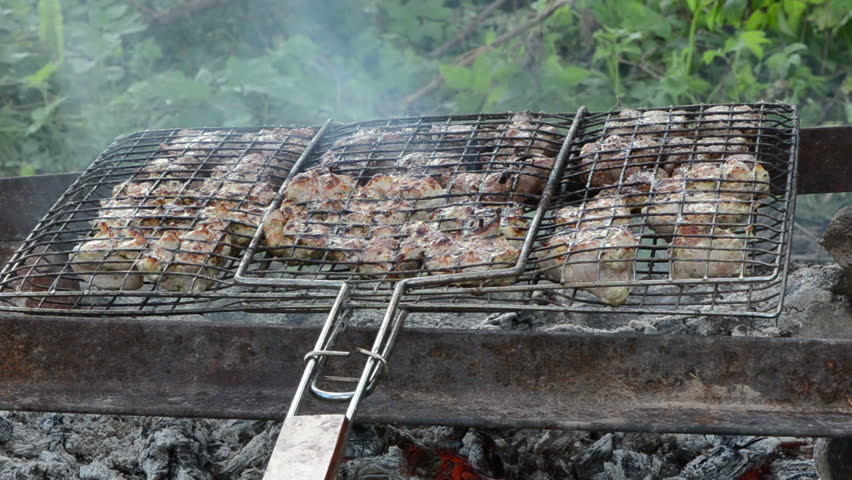 Shashlik fresh meat baked in metal grid on fireplace fire charcoal ember cinder heat.