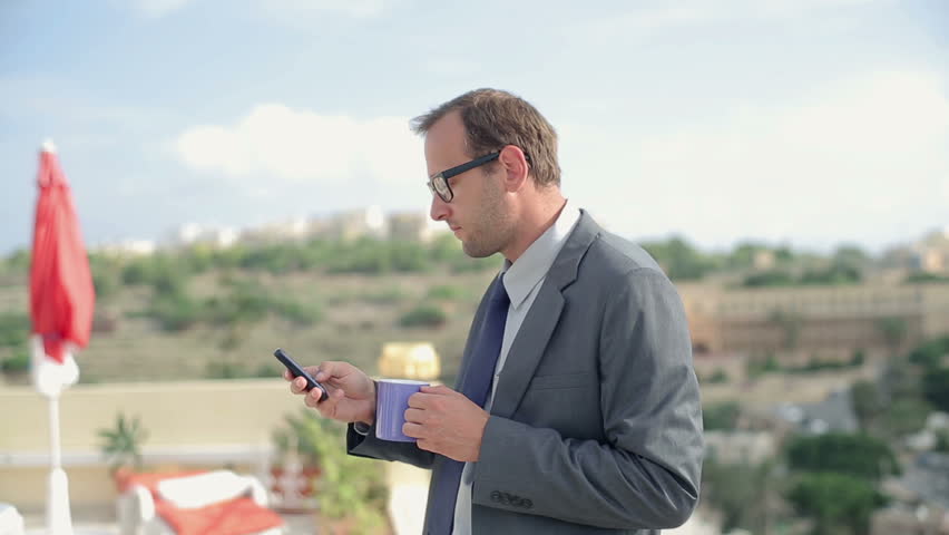 Young businessman drinking tea and using smartphone on terrace
