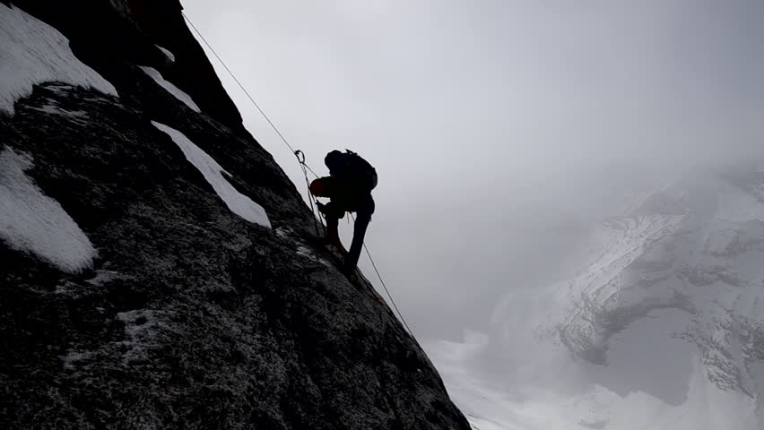 Silhouette of a climber with a backpack ascending a sheer rock face on his way to a mountain peak in the Alaskan wilderness during the day
