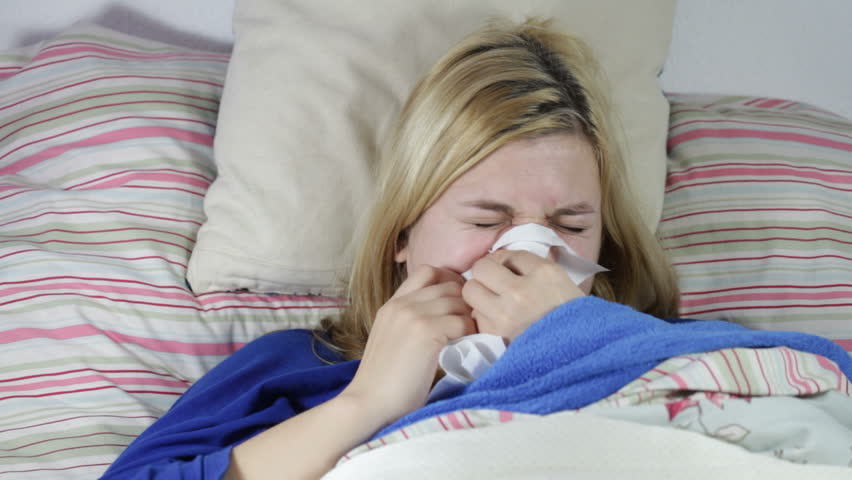 Sick woman blowing nose and sneezing in bed.