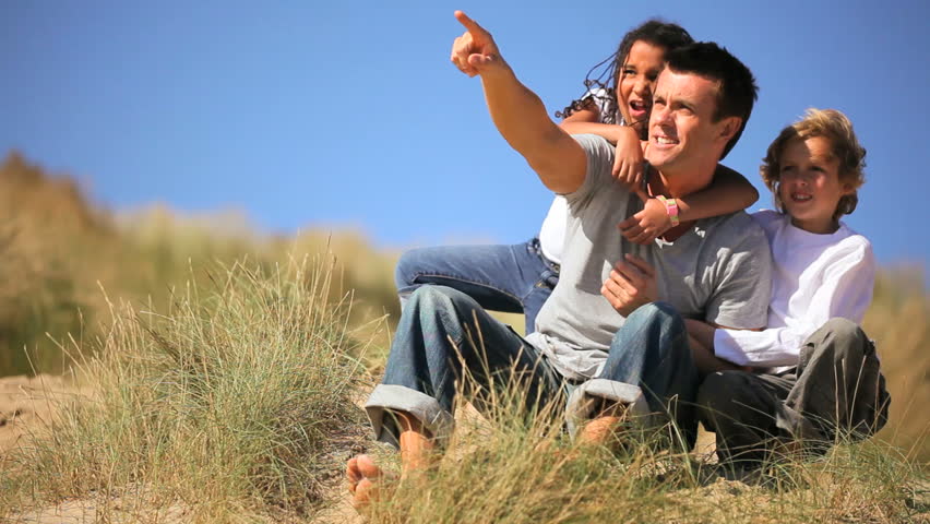 Mixed race family & friends enjoying quiet leisure time in sand dunes by the beach