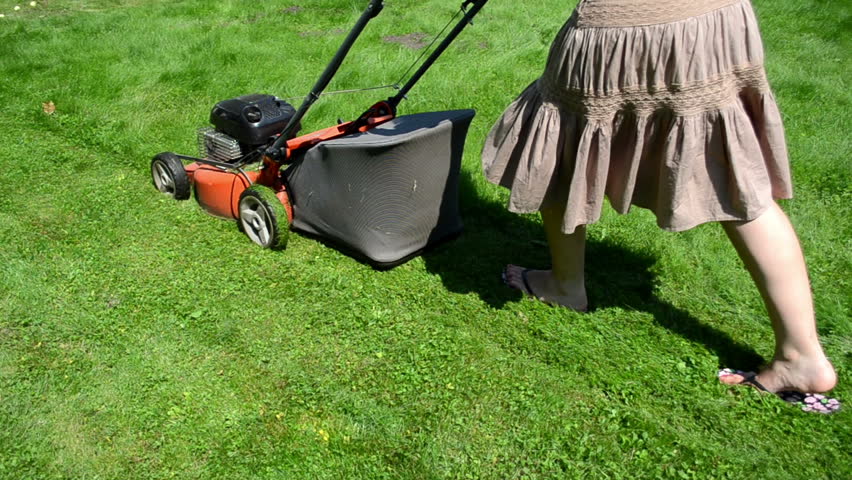 walk woman girl in skirt and flip-flop shoes cut lawn grass mower in yard.