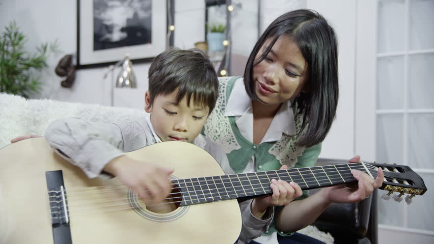 A mother gives her son a lesson in how to play the guitar