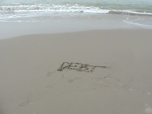 the word DEBT is washed away by the tide on the beach