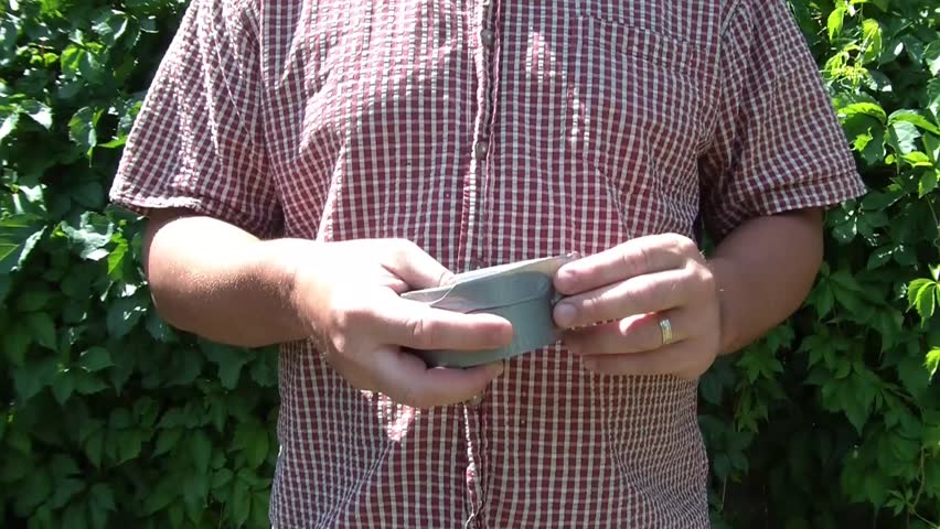 Man rips open duct tape abruptly in sunlight with natural green ivy background.