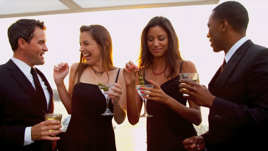 Smiling multi ethnic couples drinking and gossiping at city cocktail party dressed in black sun lens flare