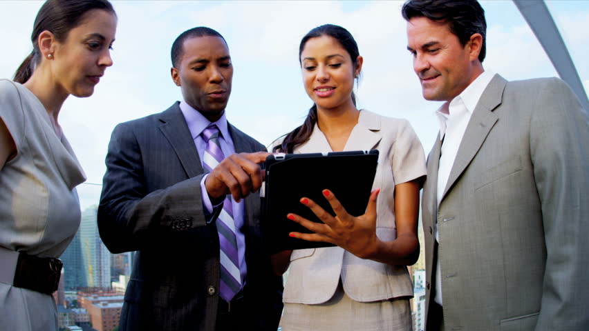 Multi ethnic male and female finance managers planning on touch screen future profit shares on rooftop overlooking city