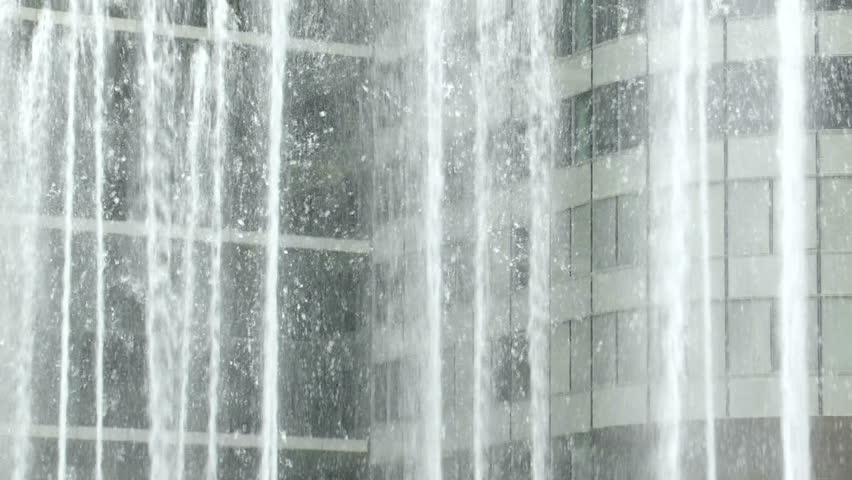 Fountain jets erupt into tall streams of water that spray, splash, obscure, city office building glass windows. 1080p