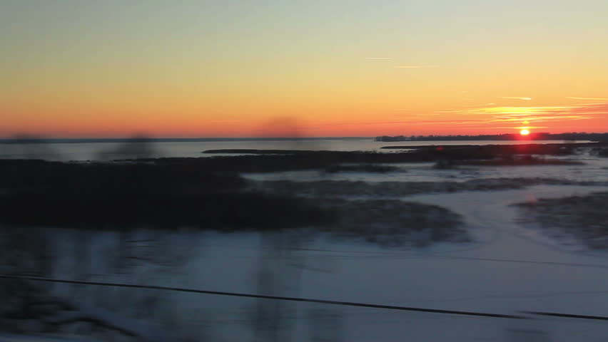Views high-speed train to the forest and the frozen lake at sunset
